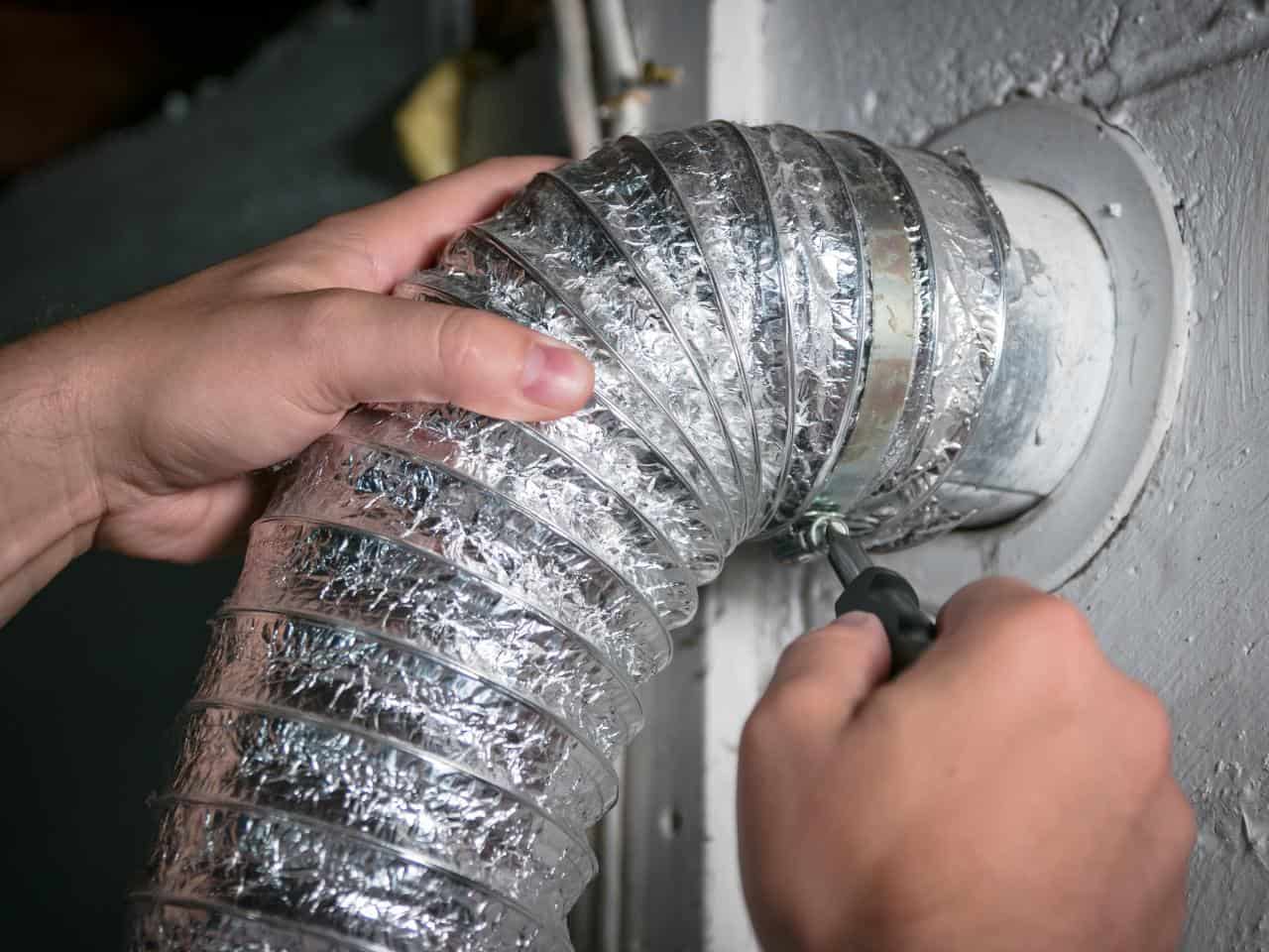 Technician installing flexible aluminum dryer vent duct in wall.