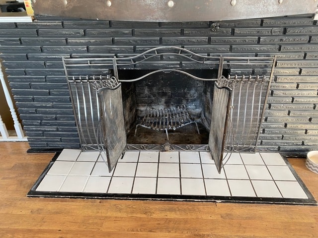 Clean and repaired fireplace with open metal doors and tiled hearth.