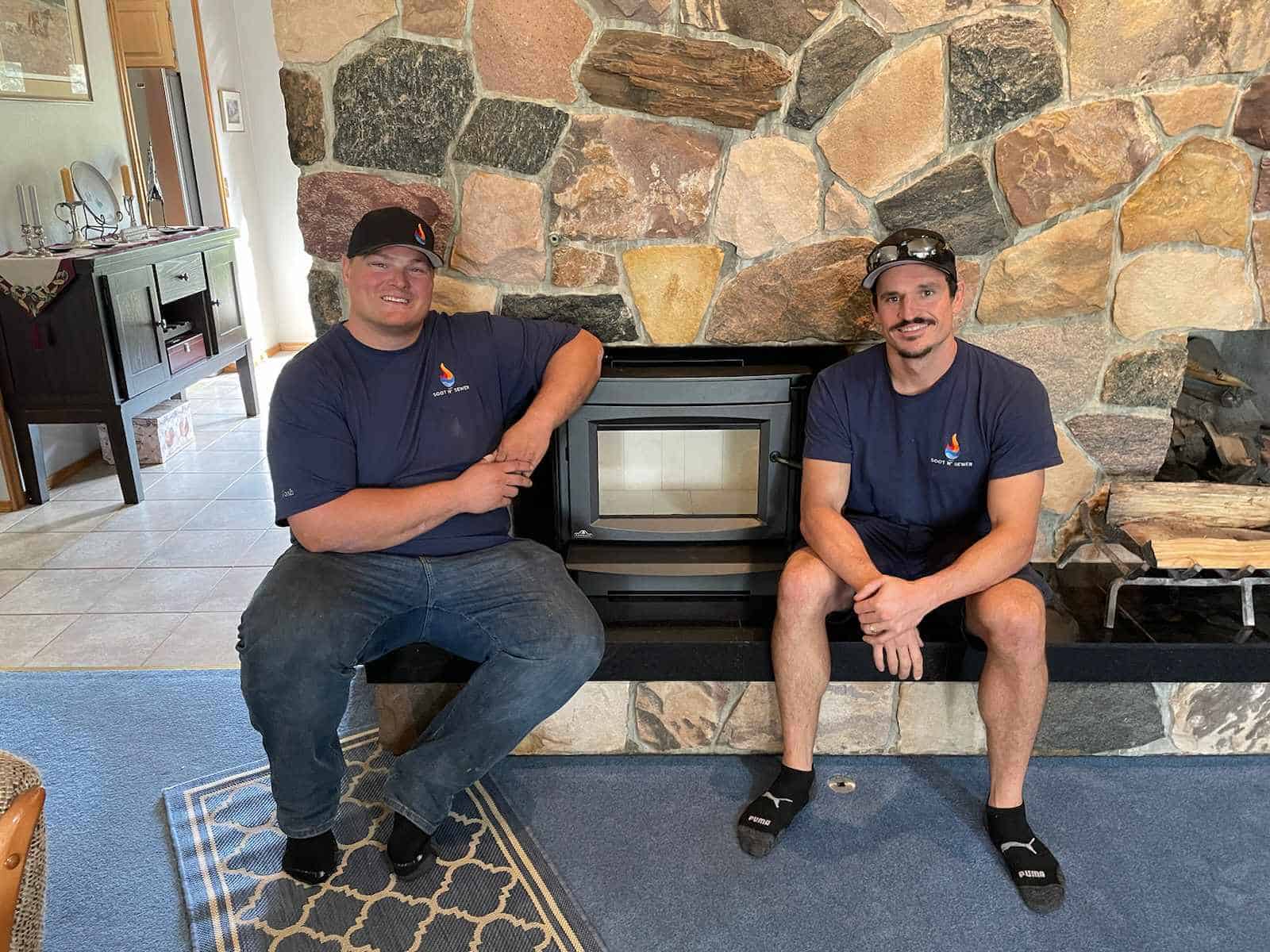 Two chimney cleaning technicians sitting by a fireplace in a home.