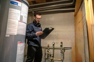 Technician inspecting a water heater in a utility room for hot water tank service.