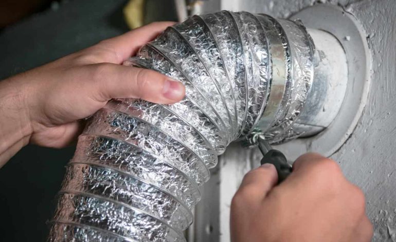 Technician installing flexible aluminum dryer vent duct in wall.
